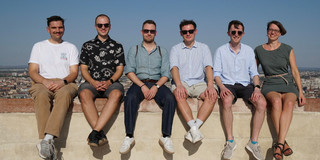 5 men and 1 woman sitting on a wall. 
