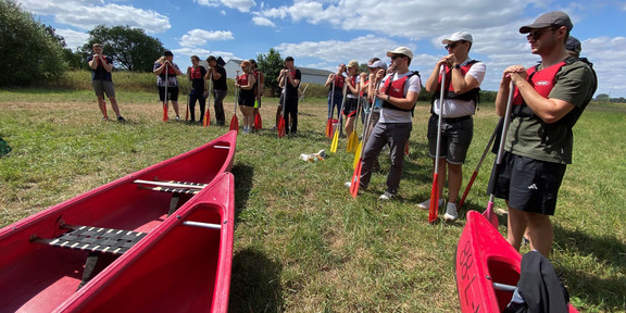 3 Canoes on the ground. Several people standing behin them.